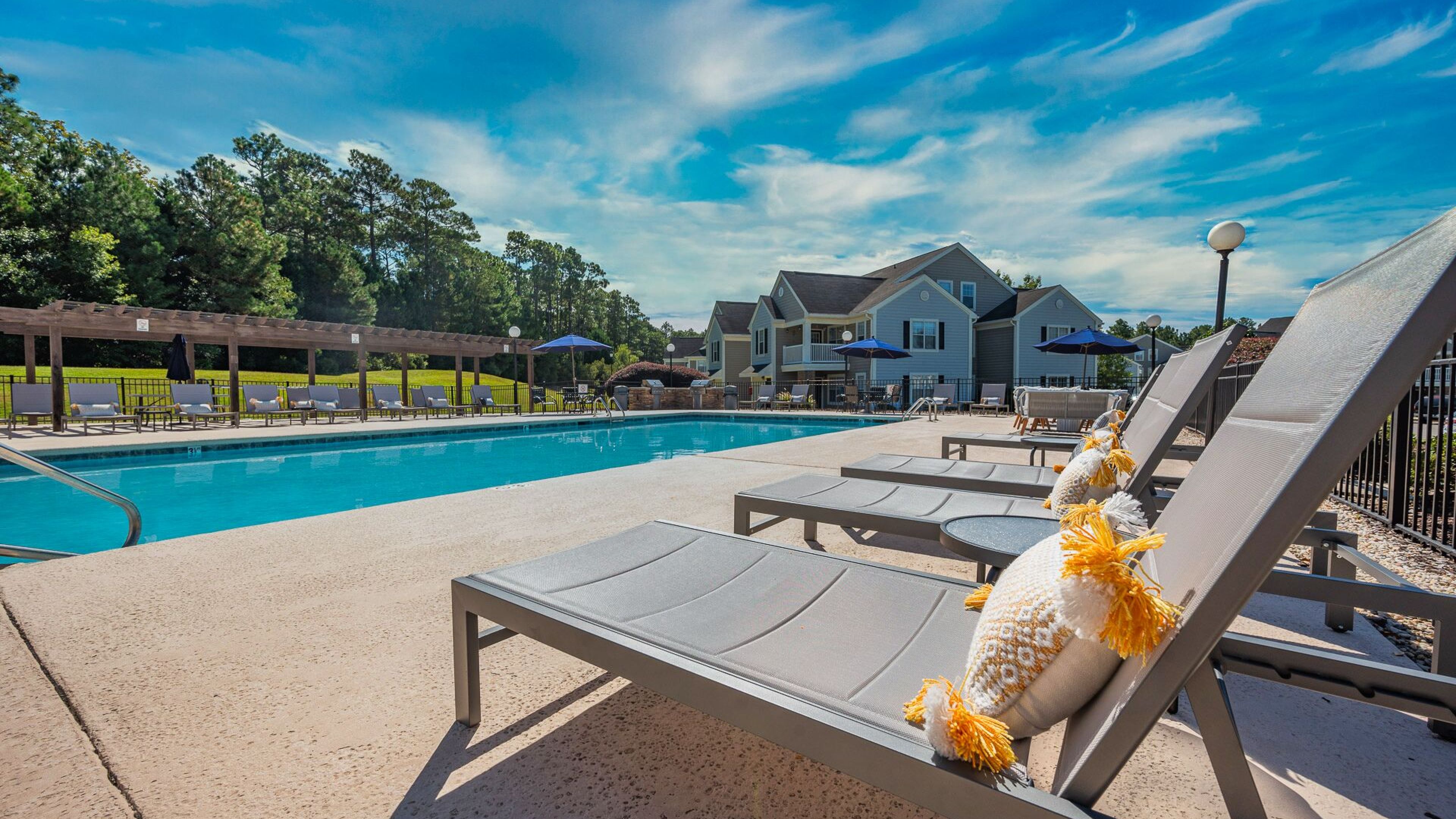 Hawthorne at the Pines poolside lounging area with comfortable sunbeds and umbrellas, overlooking a calm residential community